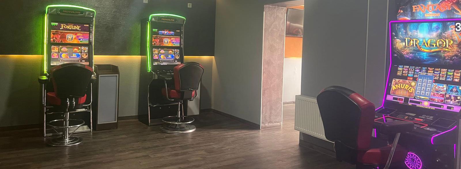 Zwei Geldspielgeräte mit grünen Leuchtrahmen an dunkler Wand in der Spielhalle Mülheim